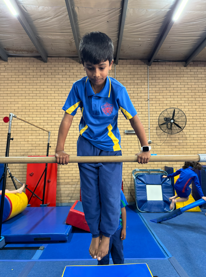 A student learning a new skill on the bar at gymnastics.